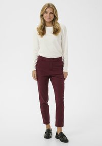 Bordové slim-fit nohavice s gombíkovým zapínaním a bočnými vreckami, skombinované s bielym topom s dlhým rukávom a čiernymi mokasínami. Hladká textúra.