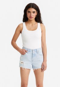 Hvid ribbet tanktop med brede stropper, parret med lyseblå slidte denimshorts med frynset kant og lommeplacering.
