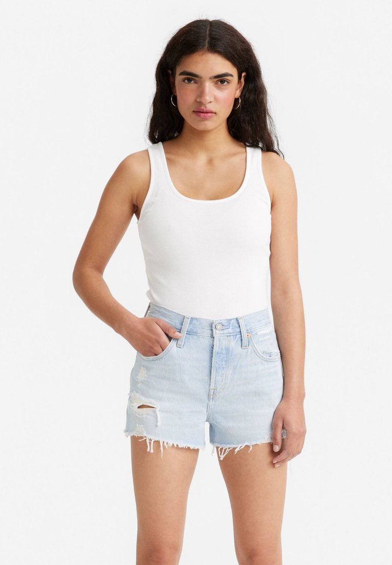 Hvid ribbet tanktop med brede stropper, parret med lyseblå slidte denimshorts med frynset kant og lommeplacering.