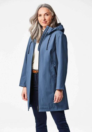 Giacca impermeabile blu con cappuccio, zip frontale e tasche laterali. Presenta maniche lunghe e una vestibilità dritta, indossata sopra un top leggero.