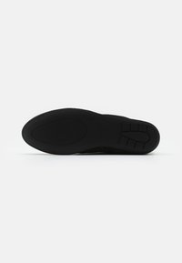 Semelle de chaussure noire avec une surface en caoutchouc texturée, présentant une forme incurvée et un design segmenté pour une meilleure adhérence et flexibilité.