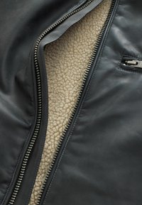 Čierna kožená bunda s béžovým fleece podšívkou, strieborným zipsom a bočnou vreckom s minimálnymi detailmi hardvéru.