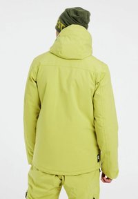 Limegrüne isolierte Jacke mit Kapuze, die eine glatte Textur und verstellbare Manschetten aufweist, kombiniert mit passenden Hosen und einer grünen Mütze.