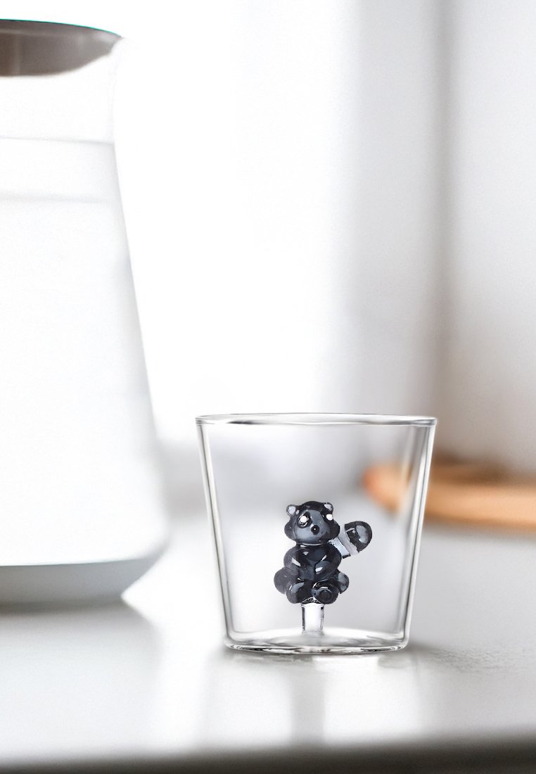 Przezroczysta szklanka z błyszczącą figurką szopa pracza w środku, z detalnymi rysami twarzy i wygiętym ogonem.