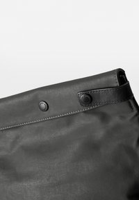 Schwarze Tasche aus glattem Material, mit einem umgeschlagenen Design, Druckknöpfen und einem Lederakzent entlang der oberen Naht.