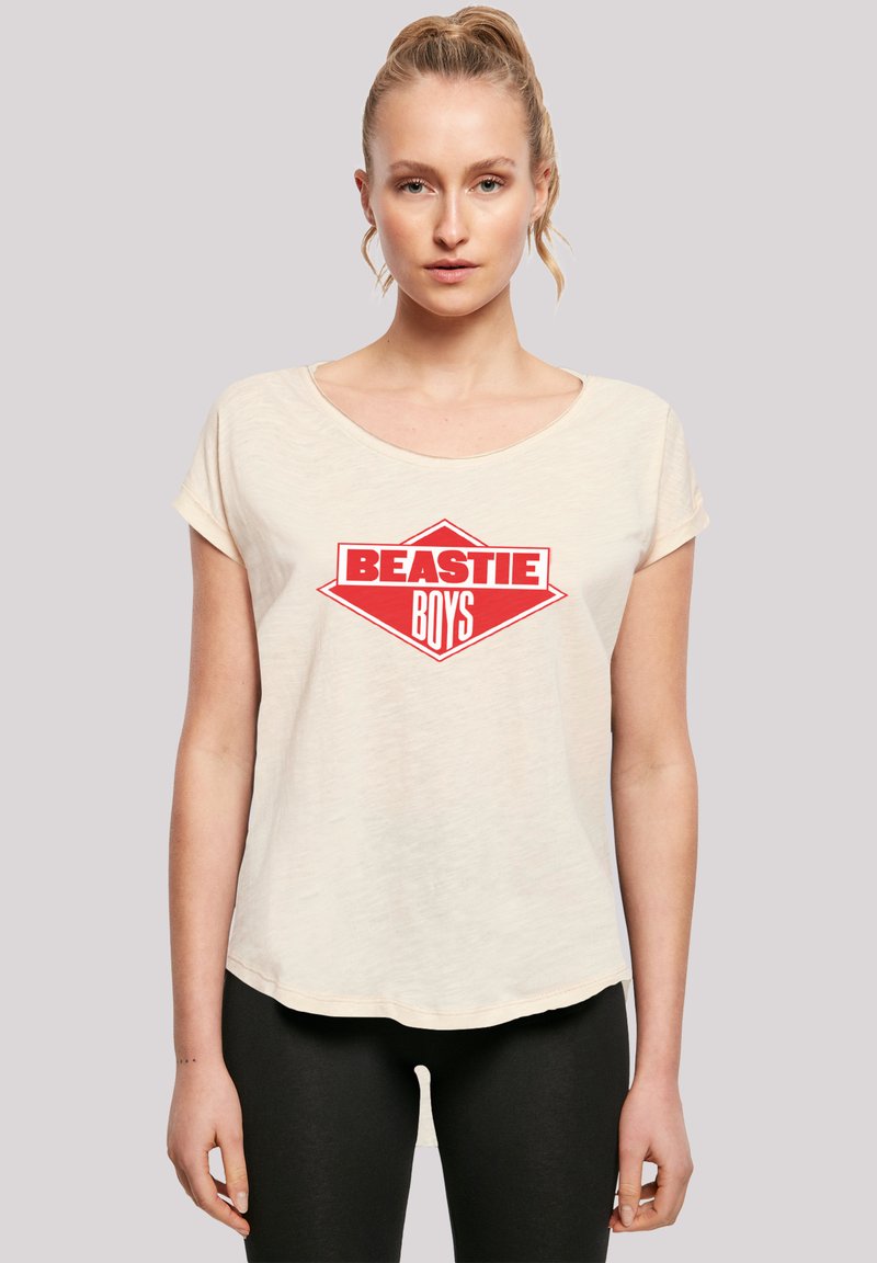 Beastie Boys T-Shirt in hellbeige, mit einem auffälligen roten und weißen Grafiklogo. Weicher Stoff, lockere Passform, leicht abgerundeter Saum und kurze Ärmel.
