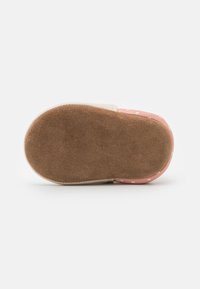 Alaa kengä, jossa on vaaleanpunainen, täplikäs kuvio, valmistettu pehmeästä mokkakankaasta. Pyöreä muoto, jonka tausta on vaaleanruskea; joustava ja teksturoidun tuntuinen.