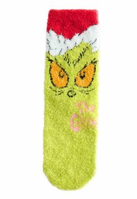 Zielona puszysta skarpeta z czerwono-białą mankietem, na której widnieje twarz Grincha z pomarańczowymi oczami oraz napisem "Grinch" w różowym haftem.
