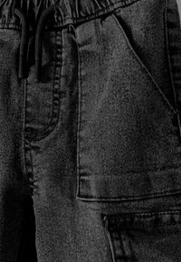 Zwart denim stof heeft een textuur oppervlakte met een elastische tailleband en trekkoord. Opvallende details zijn zijzakken en stiksels.