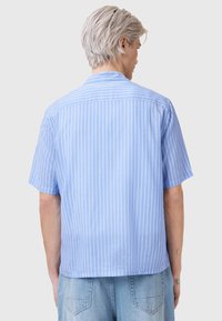 Camicia azzurra a maniche corte con bottoni, decorata da sottili strisce verticali bianche. Presenta un colletto classico e una vestibilità morbida. Materiale in cotone.