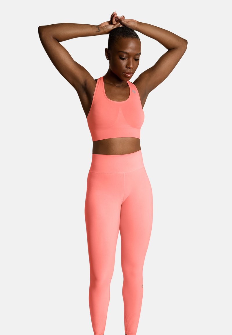 Koraliowy stanik sportowy i legginsy z wysokim stanem wykonane z gładkiego, elastycznego materiału. Prosty design z minimalną ilością hardware'u i bez widocznych wzorów.