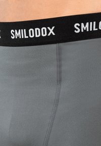 Close-up van grijze fitted stof ondergoed met een zwarte tailleband waarop de witte merktekst "SMILODOX" staat.