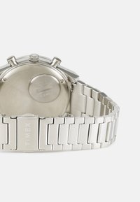Silberne Edelstahl-Uhr mit strukturierter Armbanduhr, rechteckigem Gehäuse und zwei Druckknöpfen. Mit "TIMEX" auf der Schließe graviert.