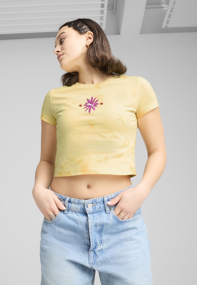 T-shirt jaune court avec broderie florale violette et étoiles sur la poitrine, associé à un jean taille haute bleu clair. Texture en coton lisse.