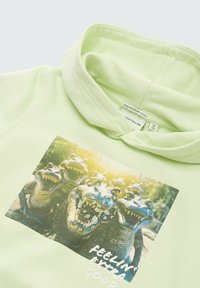 Hellgrüner Hoodie mit einer Kängurutasche und einem Grafikdesign von Alligatoren auf der Vorderseite. Das Design beinhaltet den Text "FÜHLE MICH EXTRAGEIL."