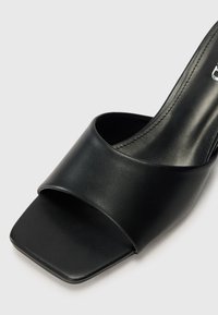 Schwarze Lederriemchensandale mit breitem oberen Riemen, quadratischer Zehenpartie und glatter Textur. Minimalistisches Design, keine sichtbaren Beschläge.