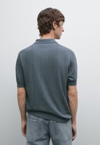 Gray knit polo shirt with short sleeves, featuring vertical stripe detailing and a ribbed collar, styled with gray denim jeans.