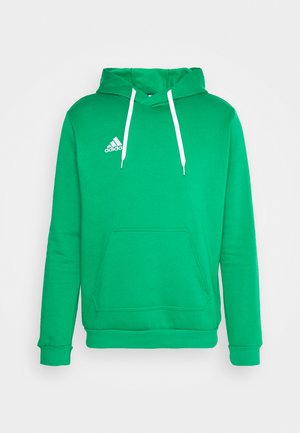 Žalias pūkinis džemperis, pagamintas iš lygaus audinio. Jame yra kengūros kišenė, baltos raišteliai ir mažas baltas logotipas ant krūtinės.