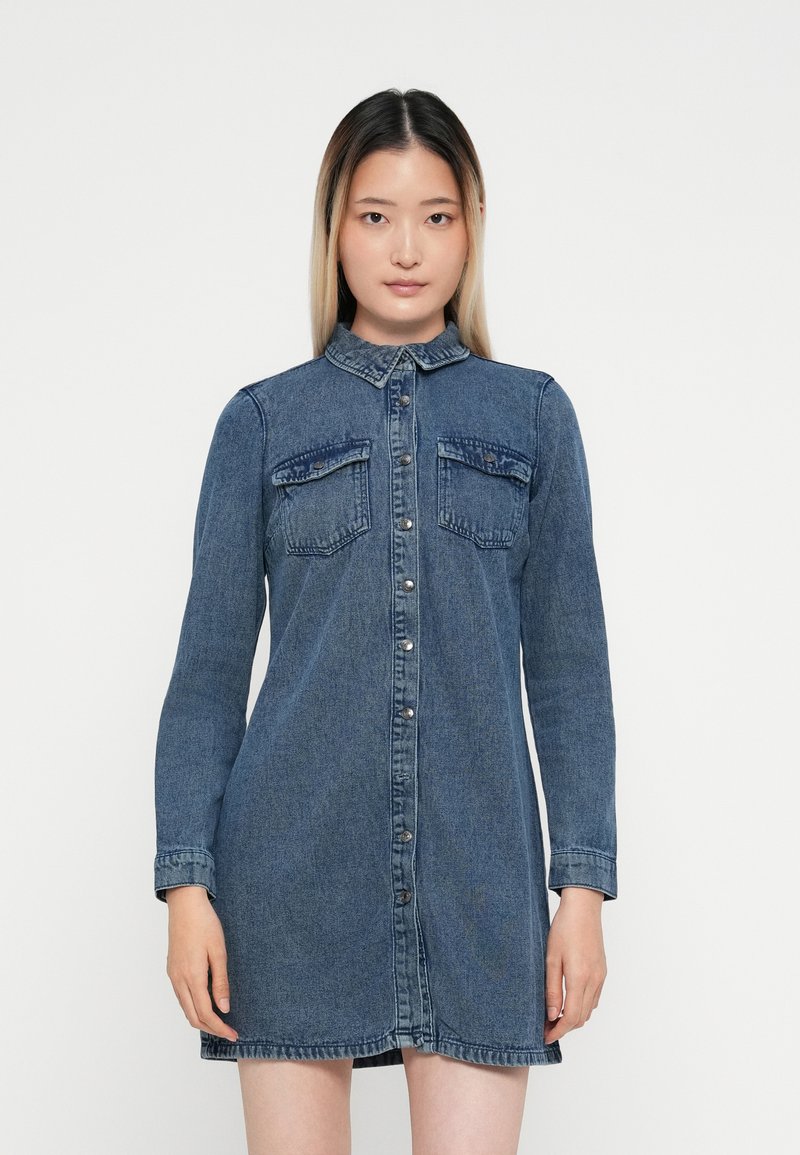 Denim krekls-kleita ar garām piedurknēm, pogu priekšpusi, diviem krūšu kabatām, apkakli un nedaudz izplestu apakšu. Krāsa: vidēji zila.