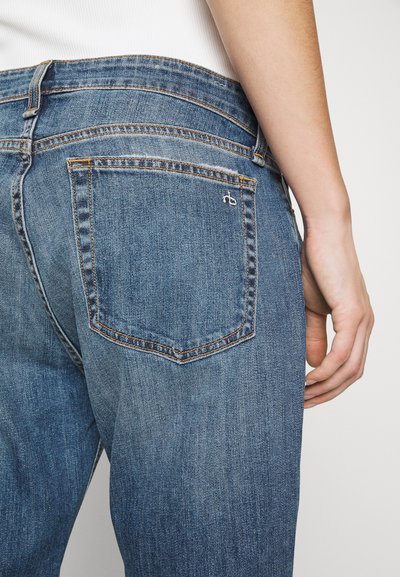 Mørkeblå denimjeans med klassisk snitt, med synlig søm, en baklomme med brodert logo, og en svakt falmet tekstur.