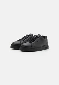 Baskets en cuir noir avec une finition lisse, bouts ronds, lacets plats et semelle en caoutchouc texturée. Design minimaliste avec des accents de marque subtils.