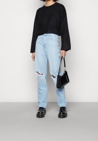 Czarny sweter z dzianiny, jasnoniebieskie dżinsy z wysokim stanem z przetarciami, masywne czarne buty oraz mała czarna torebka ze wzorem krokodyla.