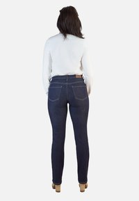 Vaqueros de denim azul oscuro con cintura alta, diseño de cinco bolsillos, bolsillos traseros y una etiqueta de cuero marrón en la cintura. Textura suave.