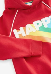 Vörös kapucnis pulóver fehér "HAPPY" felirattal és szivárványos színátmenettel. Bordás mandzsettákkal és zsinóros részletekkel rendelkezik. Puha tapintású.