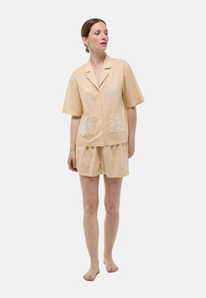 Ensemble de pyjama en tissu pêche doux, composé d'une chemise à manches courtes avec poches avant et des détails brodés blancs, associé à un short assorti.