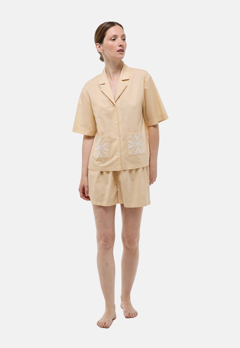 Ensemble de pyjama en tissu pêche doux, composé d'une chemise à manches courtes avec poches avant et des détails brodés blancs, associé à un short assorti.