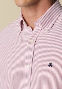 Rood-witte gestreepte overhemd met knopen en een klassieke kraag, met een marineblauw geborduurd logo op de linkerkant van de borst en een gewoven stof.