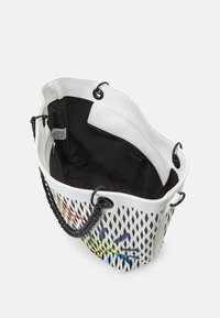 Borsa tote bianca forata con dettagli neri, dotata di un interno in tessuto nero, manico a catena e una stampa floreale colorata all'esterno.