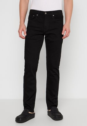 Czarne dżinsy z denimu o wąskim kroju. Posiadają szlufki na pasek, przednie i tylne kieszenie, zapinane na guziki oraz delikatne przetarcia.