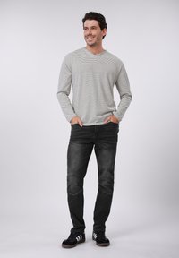 Μπλούζα μακρυμάνικη με γκρι και λευκές ρίγες και V-λαιμόκοψη, συνδυασμένη με μαύρο τζιν με λεπτομέρειες στο γόνατο και μαύρα αθλητικά παπούτσια με λευκές ρίγες.