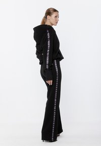 Czarny zestaw z kapturem i spodniami z białymi i fioletowymi paskami po bokach, luźny krój, miękka tkanina oraz długie rękawy z otworami na kciuki.