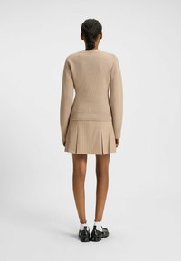 Beżowy sweter o długich rękawach, zestawiony z plisowaną beżową spódnicą z prążkami. Czarne buty z białymi skarpetkami do kostek.