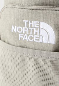 Κοντινό πλάνο μπεζ υφάσματος με λευκό κεντημένο λογότυπο "THE NORTH FACE" και υλικό από υφασμάτινο δίχτυ με υφή από κάτω.