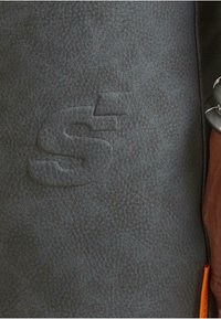 Sivá kožená taška s textúrou, s embosovaným logom a kontrastnou oranžovou visačkou, s hladkými a vzorovanými povrchovými detailmi.