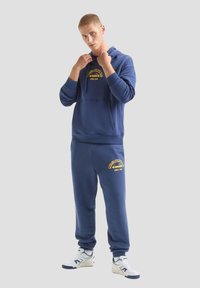 Completo felpa e pantaloni tuta blu navy, in cotone, con testo del logo giallo. Vestibilità comoda con polsini a coste e tasca frontale.