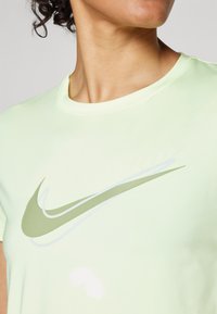 Lysegrønn Nike t-skjorte med rund hals, med et stort grønt og hvitt logodesign på forsiden. Glatt tekstur.