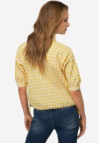 Camicia a quadri gialli e bianchi con maniche a sbuffo, orlo arricciato e dettaglio con coulisse, abbinata a jeans in denim scuro.