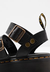 Zwarte leren sandalen met dubbele gespbanden, hardware in goudtint, gewatteerde voering en een verhoogd zwart platform met gele stiksels.