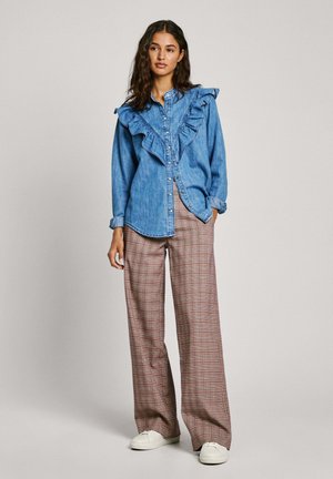 Denim shirt with ruffled front detail and button closure, paired with plaid wide-leg trousers in shades of red and beige, finished with white sneakers.