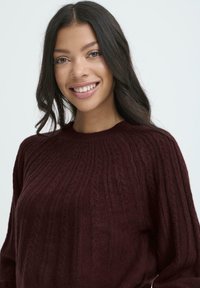 Maglione lavorato a maglia bordeaux con collo rotondo, caratterizzato da costine testurizzate e una vestibilità rilassata. Tessuto morbido e dettagli testurizzati su tutta la superficie.
