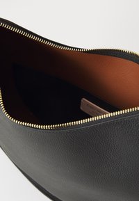 Black leather pouch with a smooth texture, gold zipper, and brown interior lining. Features a tag with brand details inside.