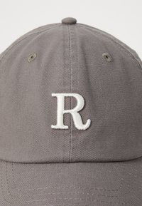 Gray cotton cap featuring a white embroidered letter "R" on the front, with a rounded crown and stitched details on the brim.