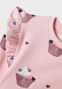 Tessuto rosa con maniche arricciate che presenta motivi di cupcake e cuori in diverse tonalità di blu, viola e rosa.