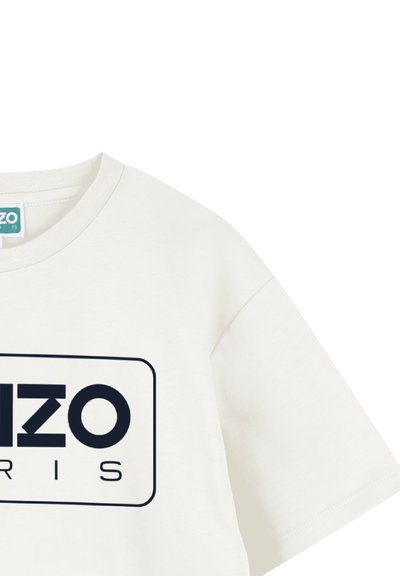 T-shirt en coton crème avec un col rond et des manches courtes. Comprend un logo bleu marine à l'intérieur d'un cadre rectangulaire à l'avant.