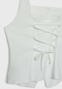 Haut blanc sans manches avec encolure carrée et détail de laçage à l'avant noué en nœud à la taille.