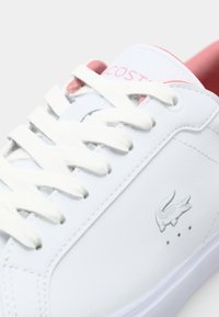 White leather sneaker with white laces, pink accents, and a gray crocodile logo. Features minimalist design and smooth texture.